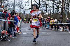 Berliner Silvesterlauf 2022: Kostümierter Läufer passiert Zuschauer in der Zielgasse @ SCC EVENTS / Tilo Wiedensohler