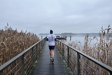 Berliner Silvesterlauf: Mann trainiert bei Kälte und läuft einen Steg entlang, Richtung See © SCC Events